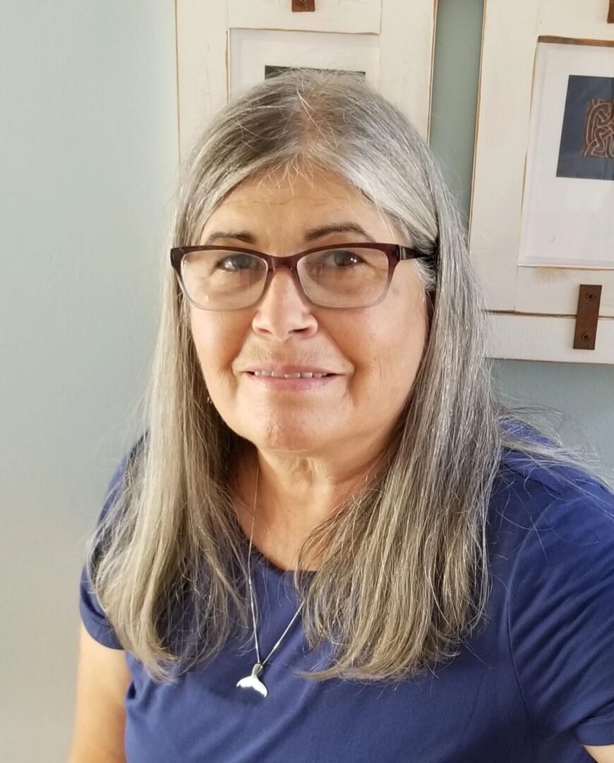 A woman with long gray hair wearing glasses.
