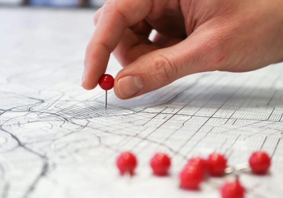 Hand placing a red pin on a map.