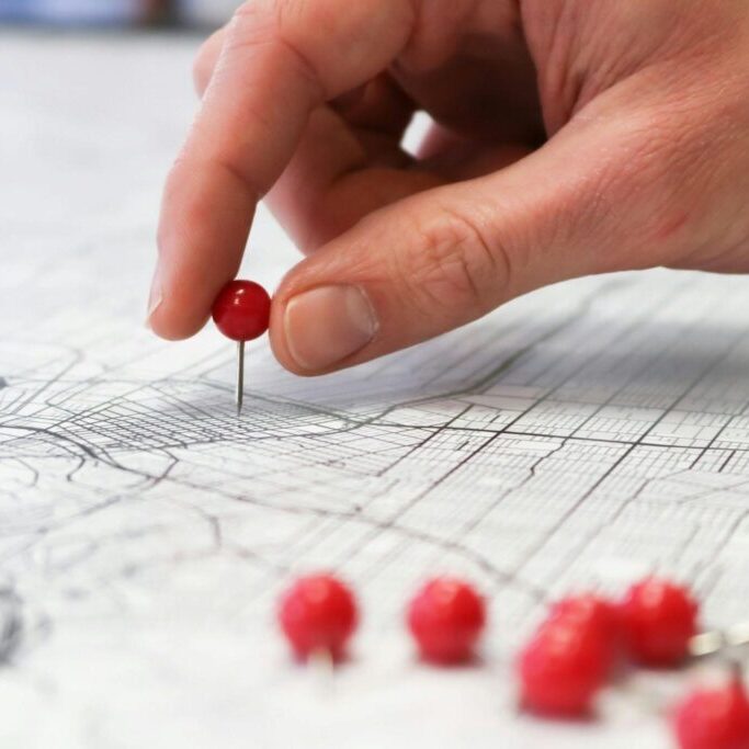 Hand placing a red pin on a map.